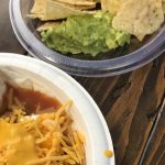 A zoomed in photo of a fajita covered in cheese, along with chip and guacamole.